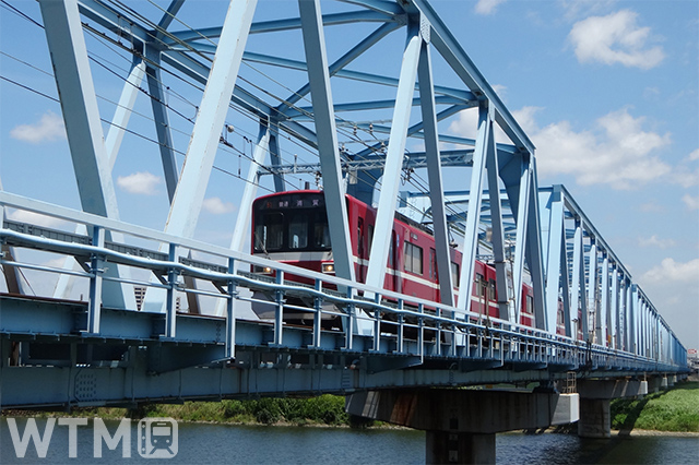 都県境の多摩川に架かる六郷川橋梁を渡る京急1500形電車(ponpokopon/写真AC)